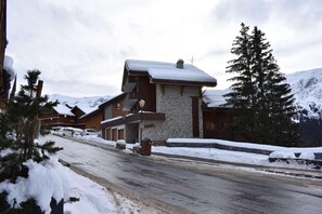 A snow-covered mountain lodge with stone and wood architecture, a paved road, and a clear sky. - 100m from ski lifts, 1st floor, tv, ski locker, 65m², Méribel (Méribel - Les Allues)