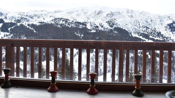 A wooden balcony railing with a view of snow-covered mountains and trees.