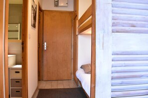 Un pasillo estrecho con una puerta de madera, una cama con cabecero y un baño pequeño con inodoro y cajones para guardar cosas.