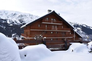 Una cabaña de madera con varios balcones, al pie de una montaña nevada.