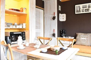 Un comedor con una mesa de madera dispuesta para dos personas, una cafetera y una estantería con vajilla y tazas.