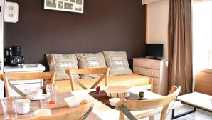 A hotel room with a bed, a desk with a coffee maker, a television, and a dining area with chairs and a table.