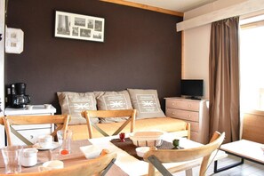 Habitación de hotel con cama, escritorio con cafetera, televisor y zona de comedor con sillas y mesa.