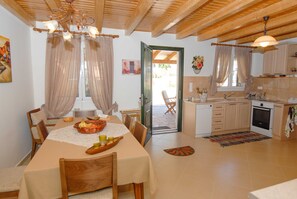 A dining area with a table set for four, a kitchen with white cabinets, and a door leading outside.