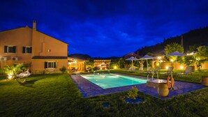 Ein Nachtbild eines Wohnhauses mit Swimmingpool, Sitzgelegenheiten im Freien und einem gut beleuchteten Patio.
