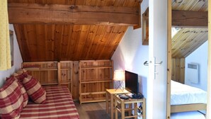 Une pièce chaleureuse avec un plafond en pente, des meubles en bois, un lit, un bureau avec un ordinateur et une fenêtre.