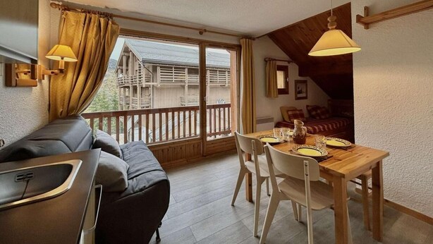 Une pièce chaleureuse avec un canapé, une table à manger et des chaises, un plafond en bois et un balcon doté d’une balustrade.