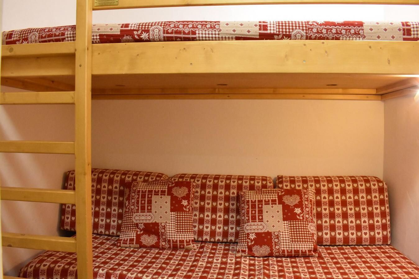 A bunk bed with a checkered red and white pattern, a wooden ladder, and a lower bunk with matching pillows.