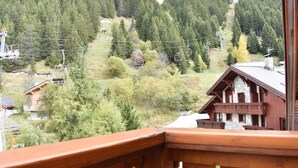 Un chalet en bois doté d’un balcon, entouré d’une colline boisée et avec un télésiège visible au loin.