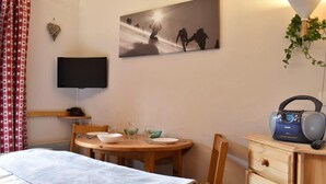 Une chambre d’hôtel comprenant un lit, une table à manger avec des chaises, un téléviseur, un tableau, une radio et une plante.