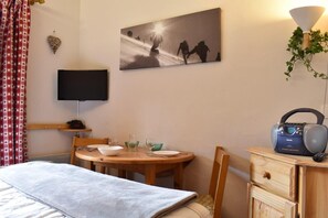 A hotel room with a bed, a dining table with chairs, a television, a painting, a radio, and a plant. - 300m from shops, 1st floor, balcony, tv, ski locker, 18m², Méribel (Méribel - Les Allues)