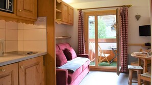 Une cuisine compacte avec des meubles en bois et un micro-ondes encastré, un confortable canapé rouge et un coin repas avec une table et des chaises.