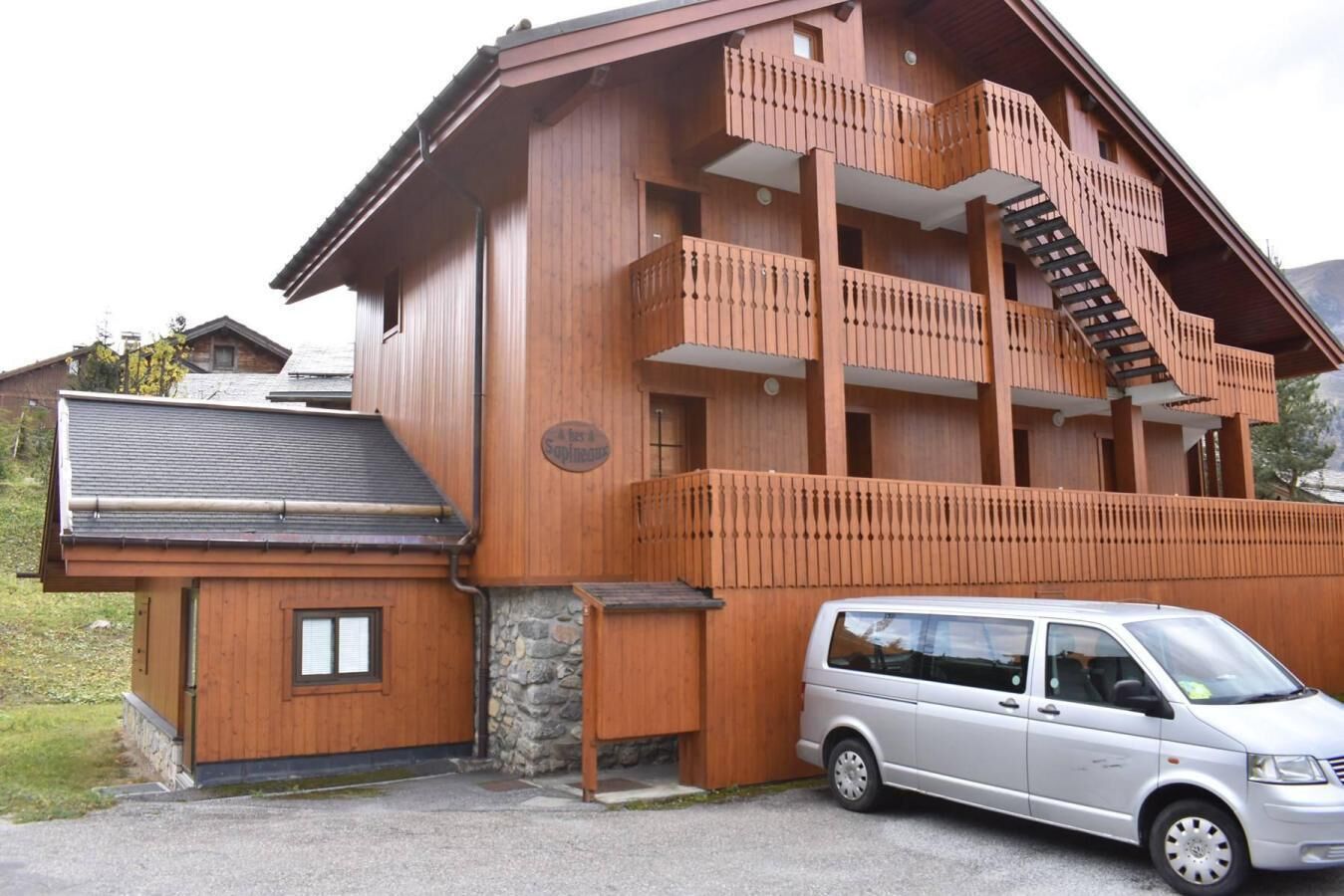 A multi-story wooden building with a stone foundation, a small attached structure, and a staircase leading to the upper floors.