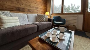 A cozy room with a wooden wall, a grey sofa with patterned cushions, a blue chair, and a tray with cups and saucers.