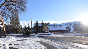 Carretera nevada que lleva a un edificio con una escultura de bola de nieve, rodeado de árboles y montañas.