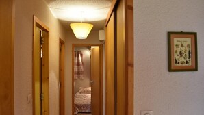 Un estrecho pasillo con puertas de madera que conducen a un dormitorio con colcha estampada.
