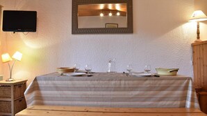 Un comedor con una mesa dispuesta para dos, un televisor montado en la pared y una lámpara al lado.
