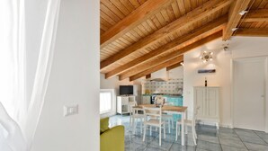 Eine moderne Küche mit Holzbalkendecke, einem Essbereich mit weißen Stühlen und einem grünen Sofa.