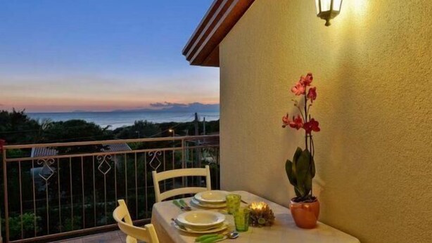 Ein Balkon mit Tisch für zwei Personen, einer Topforchidee und Blick auf das Meer im Dämmerlicht.