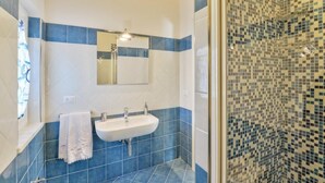 Ein Badezimmer mit einem weißen Waschbecken, zwei Wasserhähnen, einem Spiegel und einer Dusche mit Mosaikfliesen.