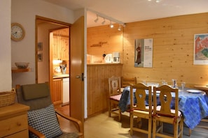 A cozy room with wooden walls, a dining table set for four, and a kitchen area visible through an open door. - 150m from shops, 2nd floor, balcony, tv, ski locker, 50m², Méribel (Méribel - Les Allues)