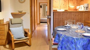 Une pièce chaleureuse avec une table à manger en bois, mise pour deux personnes, une chaise en bois avec un coussin et un buffet en bois contenant une bouilloire et une machine à café.
