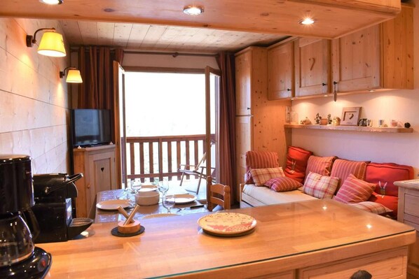 A cozy cabin interior with a wooden dining table, a sofa, and a kitchen area with a coffee maker.