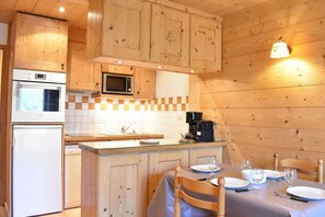 A compact kitchen with wooden cabinets, a microwave, a coffee maker, and a dining area with a table set for two.