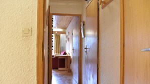 Ein Flur mit einer Holztür rechts, einem kleinen Tisch mit Lampe und einem Bett im Hintergrund.