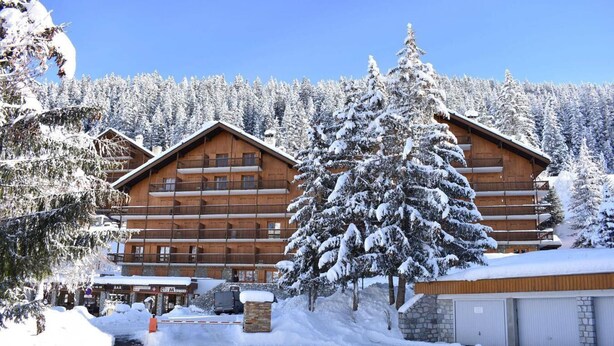 Un chalet en bois doté de plusieurs balcons, entouré d’arbres couverts de neige et surplombant un ciel dégagé.