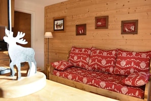 A wooden wall with framed pictures, a sofa with patterned cushions, and a reindeer decoration. - 50m from shops, 1st floor, balcony, tv, 16m², Méribel (Méribel - Les Allues)