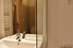 Features a large mirror above a sink, a shower area, and a wooden door.