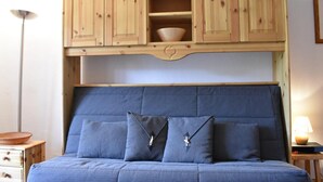 A bedroom with a blue bed, wooden cabinets above the bed, and a bedside table with a lamp. - 100m from ski slopes, 3rd floor, balcony, tv, 28m², Méribel (Méribel - Les Allues)