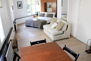 Quarto moderno e bem iluminado com uma cama, sofá, mesa de jantar e televisão.
