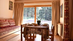 A cozy room with a wooden ceiling, a dining table set with plates and a green vase, a sofa with patterned cushions, and a window with curtains. - 150m from shops, Ground floor, terrace, ski locker, 40m², Méribel (Méribel - Les Allues)