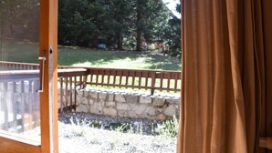 A view from a room with a stone wall and a wooden deck leading to a grassy yard with trees. - 150m from shops, Ground floor, terrace, ski locker, 40m², Méribel (Méribel - Les Allues)