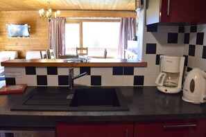 Una cucina con zoccolo a scacchi bianco e nero, piano di lavoro in legno, lavello, macchina per il caffè e televisore montato a parete.