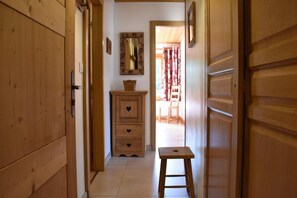 Ein schmaler Korridor mit Holztüren und einem kleinen Hocker. Ein Holzschrank mit herzförmigen Griffen ist zu sehen.