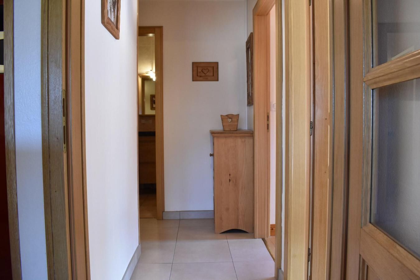 A narrow hallway with wooden doors and a tiled floor.