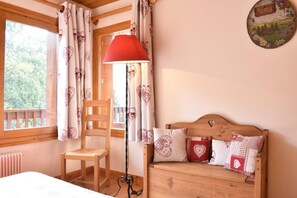 Una camera accogliente con un letto di legno, una sedia, una lampada da terra rossa e una finestra con tende.