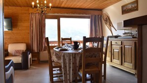A cozy dining area with a wooden table set for four, surrounded by chairs. A chandelier hangs from the ceiling, and a television is mounted on the wall. - 100m from ski slopes, 2nd floor, balcony, ski locker, 60m², Méribel (Méribel - Les Allues)