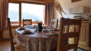 A dining area with a table set for four, wooden chairs, a view of mountains through large windows, and a painting on the wall. - 100m from ski slopes, 2nd floor, balcony, ski locker, 60m², Méribel (Méribel - Les Allues)