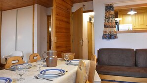 A dining area with a table set for four, a wooden ceiling, a sofa, and a kitchen visible through an open door.