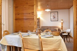 Zona pranzo con arredamento in legno, un tavolo apparecchiato con piatti e bicchieri e un divano sullo sfondo.