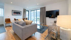 Ein modernes Wohnzimmer mit einem grauen Sofa, einem Couchtisch und einem an der Wand befestigten Fernseher.