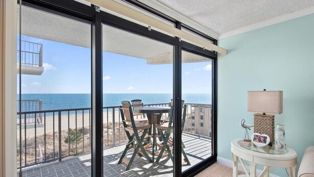 Un balcone con tavolo e sedie, un piccolo tavolino con lampada e vista sull'oceano.