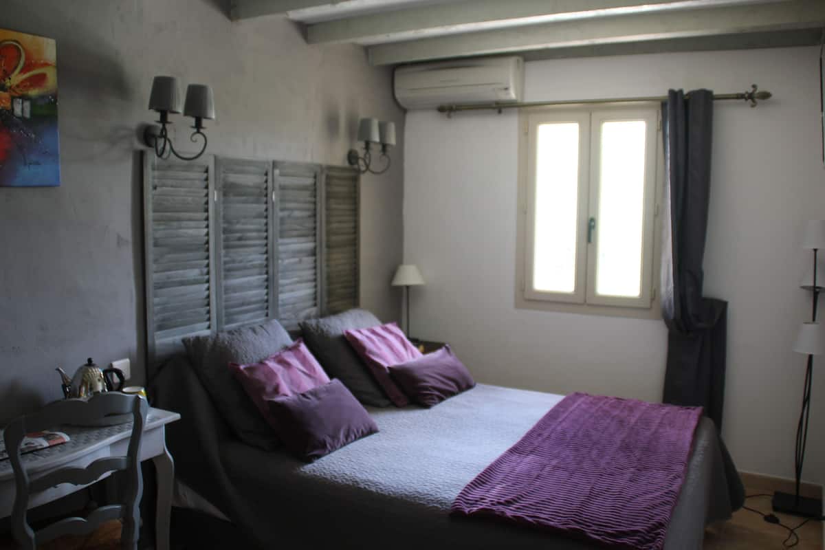A bedroom with a bed, bedside table, lamp, and window with curtains.