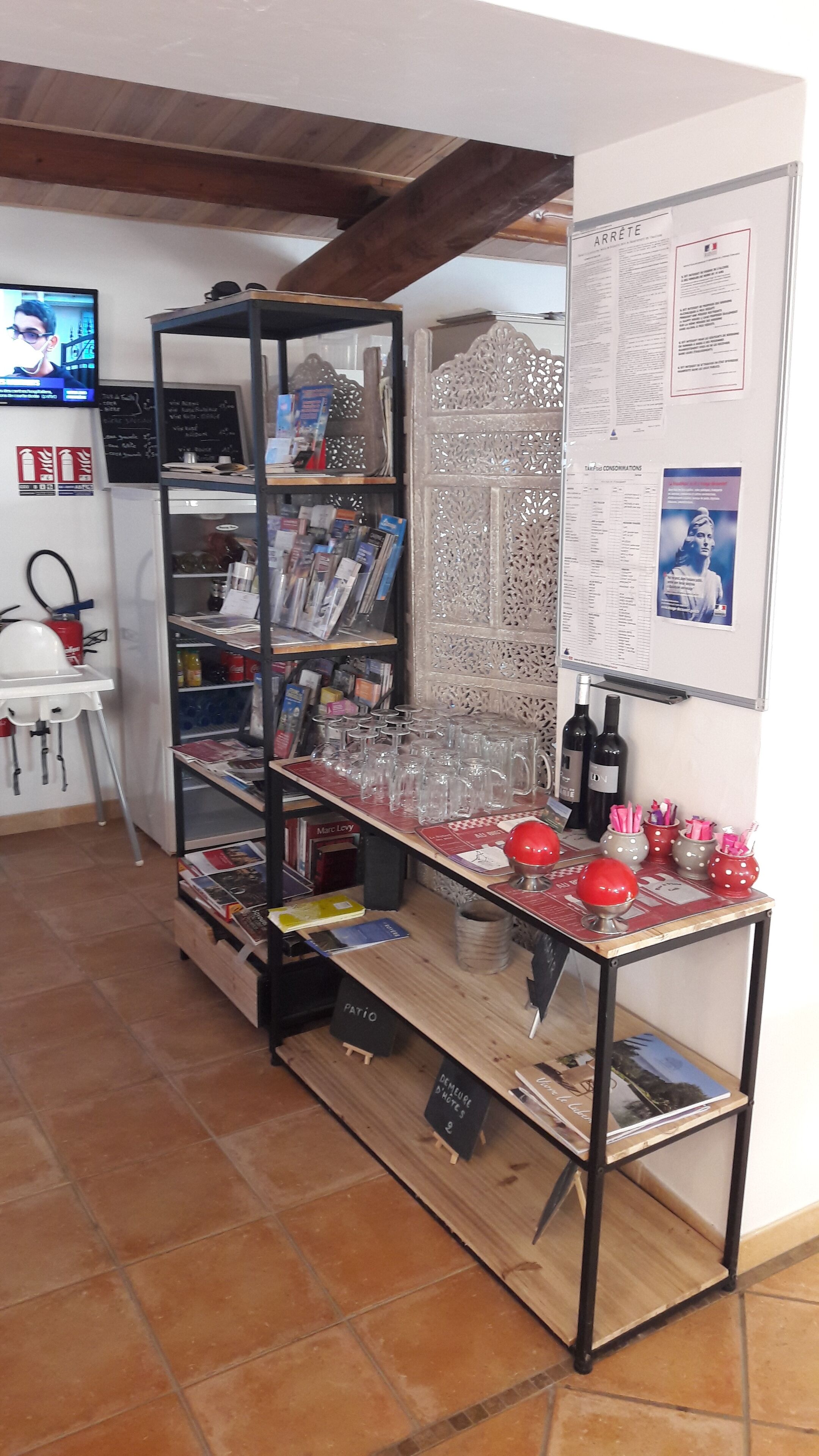Una habitación con una mesa de madera, estantes con libros y revistas, un extintor y una pizarra con escritura.