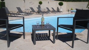 A poolside area with lounge chairs and a table with a bottle and glasses. - Mas Dansavan (Oppede)