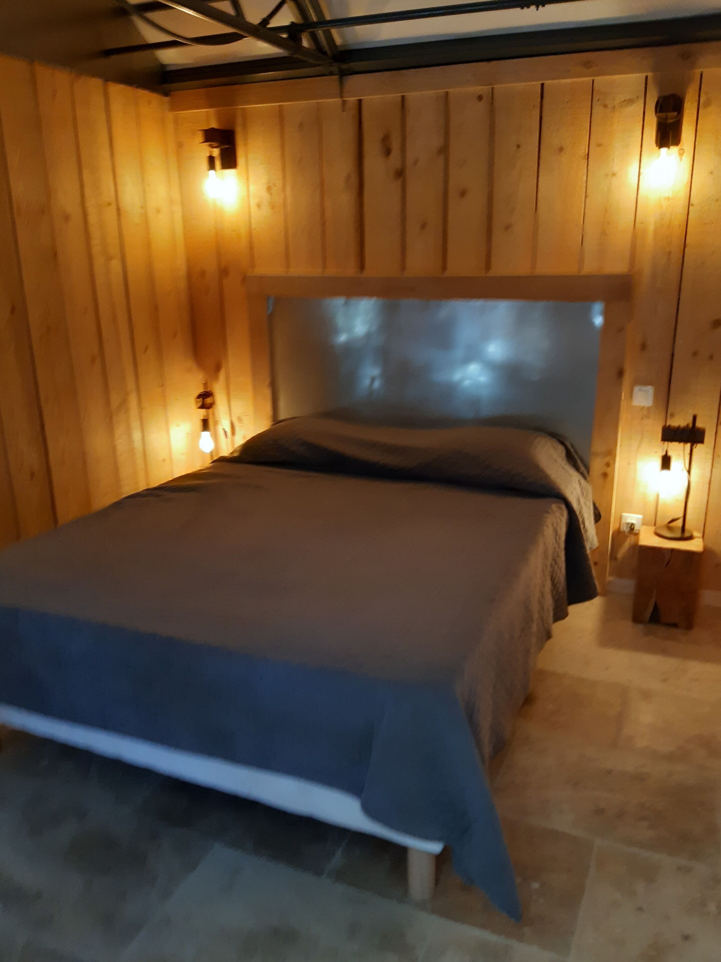 Un dormitorio con paneles de madera, una cama, dos lámparas de noche y una mesita de noche pequeña de madera.